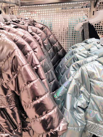 warm jackets of light silver blue hang on a hanger in a store, winter clothes sale. jackets hanging...