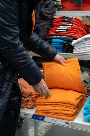 15.03.2020 Moscow, Russia. the girl chooses an orange t-shirt from a stack of t-shirts of different sizes stacked in the store. concept shoppingのeditorial素材