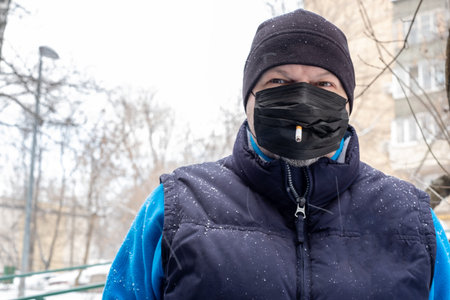 Smoking. Closeup man with mask during COVID-19 pandemic smoking a cigarette at the street. a man in...