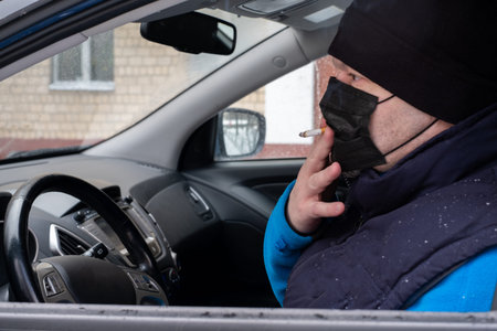 Smoking. Closeup man with mask during COVID-19 pandemic smoking a cigarette at the street.a man in a...