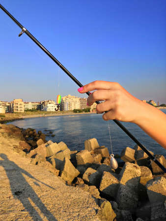 women's hands impaling a worm on a hook on a fishing trip. Close-up of the hands of a fisherman who impales worms on the hook of a fishing rod on a wooden pier.の写真素材