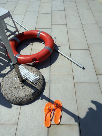 Lifeguard equipment, orange lifebelt with rope hang on the wall near the swimming pool.