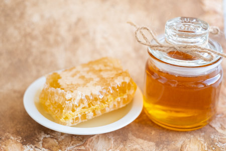 glass jar full of honey, plate with honeycomb on light brown backgroundの写真素材