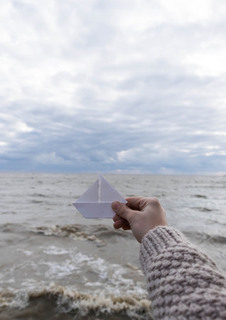 Close-up of human hand paper boat sea backroundの写真素材