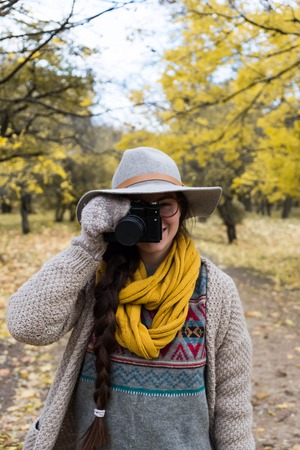 GIrl in gray hat taking pictures with a professional camera at the autumn parkの写真素材