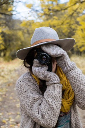 GIrl in gray hat taking pictures with a professional camera at the autumn parkの写真素材