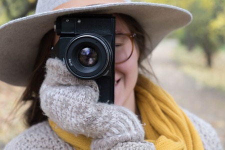 GIrl in gray hat taking pictures with a professional camera at the autumn parkの写真素材