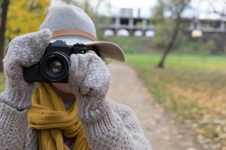GIrl in gray hat taking pictures with a professional camera at the autumn parkの写真素材