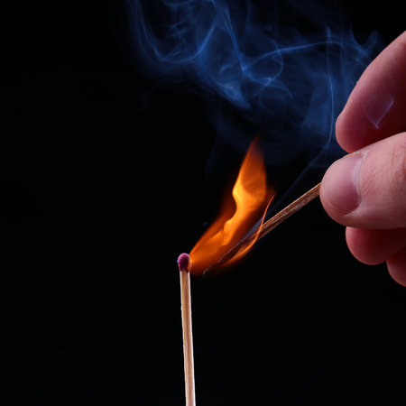 Ignition of a match, with smoke on dark background. Hand holding burning match stick