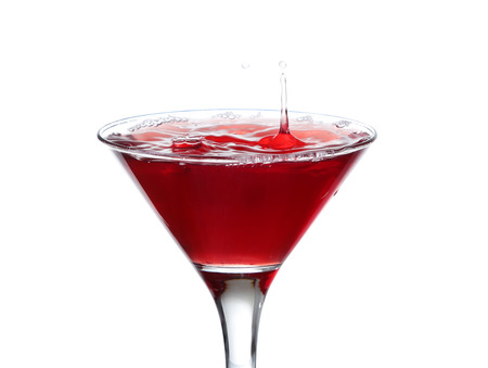 A martini glass on a white background; the water ripples and splashed as a green spanish olive with pimento is dropped into the glass; horizontal formatの写真素材