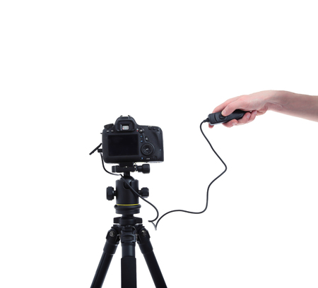 Camera with the lens on tripod. Hand presses the shutter or remote control unitの写真素材