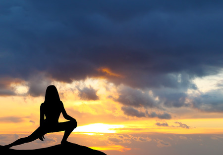 Silhouette of woman practicing yoga during sunset at the seaside.の写真素材
