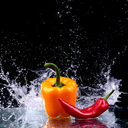 Studio shot with freeze motion of peppers in water splash on black backgroundの写真素材