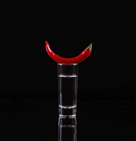 Shot of vodka with chili peppers on a black backgroundの写真素材