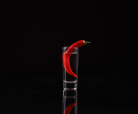 Shot of vodka with chili peppers on a black background