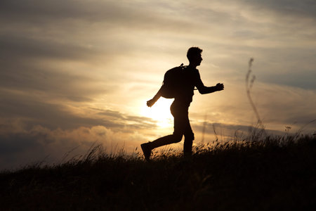 Man runs directly on a hill against a beautiful sunset
