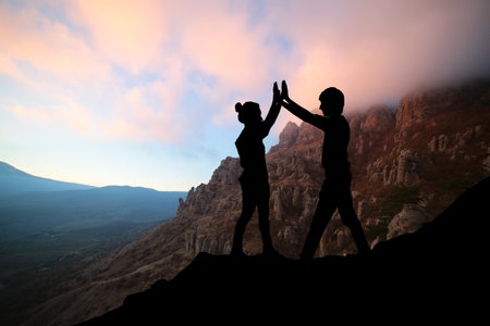 Male and female hikers climbing up mountain cliff and one of them giving helping hand. People...