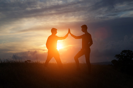 Male and female hikers climbing up mountain cliff and one of them giving helping hand. People helping and, team work concept.の写真素材