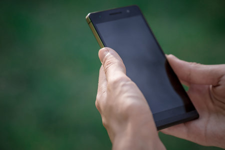 hand hold black smart phone, cell phone, mobile over blurred image of green forest background