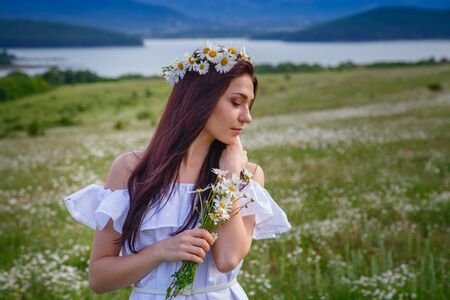Beautiful woman enjoying daisy field, nice female lying down in meadow of flowers, pretty girl relaxing outdoor, having fun, holding plant, happy young lady and spring green nature, harmony conceptの写真素材