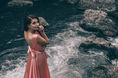 Young woman in gorgeous pink dress with waving flying fabric, fashion female posing in the park, near the riverの写真素材
