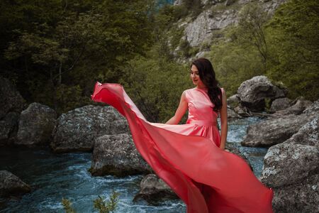 Young woman in gorgeous pink dress with waving flying fabric, fashion female posing in the park, near the riverの写真素材