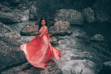 Young woman in gorgeous pink dress with waving flying fabric, fashion female posing in the park,...