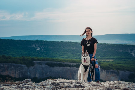 Beautiful girl plays with a dog grey and white husky in the mountains at sunset, summer mood, happy...