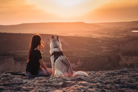 Beautiful girl plays with a dog - grey and white husky in the mountains at sunsetの写真素材