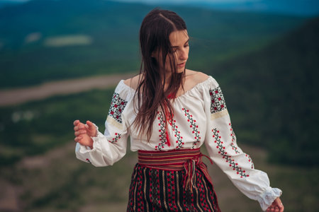 Atractive woman in traditional romanian costume on mountain green blurred background. Outdoor photo....
