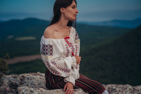 Atractive woman in traditional romanian costume on mountain green blurred background. Outdoor photo....