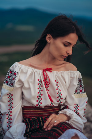 Atractive woman in traditional romanian costume on mountain green blurred background. Outdoor photo....
