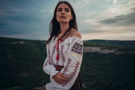 Atractive woman in traditional romanian costume on mountain green blurred background. Outdoor photo. Traditions and cultural diversityの写真素材