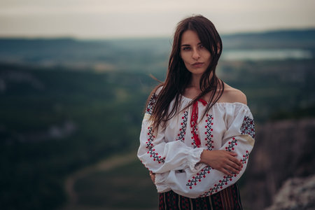Atractive woman in traditional romanian costume on mountain green blurred background. Outdoor photo. Traditions and cultural diversityの写真素材