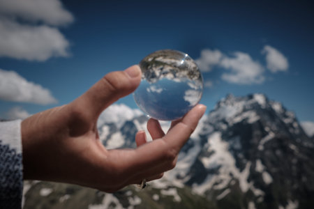 Concept and idea of travel. snow peaks of the alps seen through a glass sphere hold by a hand