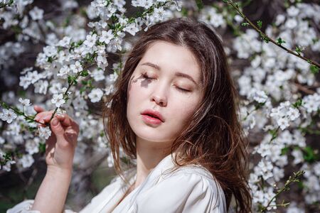 young asian woman in a flowering garden. romantic image of stylish casual woman , trendy silk blouse. positive mood. Cheery Blossom full bloom in Japan.の写真素材