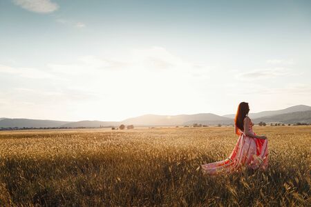 girl dancing in a field in a beautiful pink dress at sunset. ideal for advertising and photo sun shines bright and juicyの写真素材