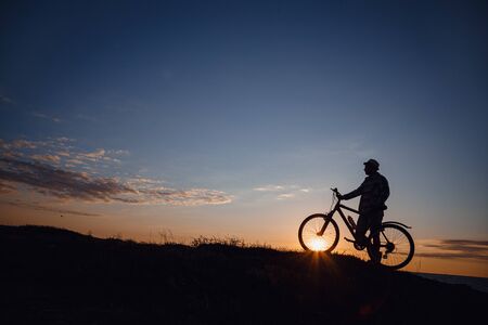 silhouette of a hipster man on a bicycle on sunset background. Idea and concept of physical activity and healthy lifestyleの写真素材
