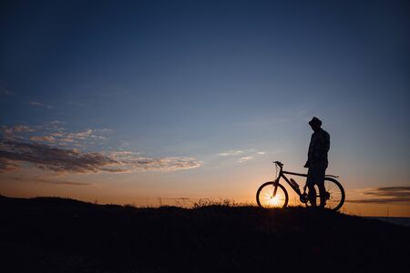 silhouette of a hipster man on a bicycle on sunset background. Idea and concept of physical activity and healthy lifestyleの写真素材