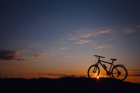 silhouette of a bicycle on the sunset sky. wonderful rural countryside. Weekend in fresh air, among nature.の写真素材