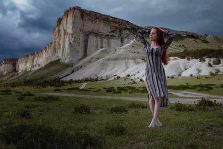 fashion young ginger woman standing outdoor on breathtaking view of dramatic storm sky in the field. Crimea, White Rock near Belogorskの写真素材