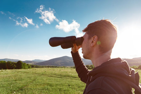 Young man at mountain looking through binoculars. Banner with copy space. idea and concept of travel...