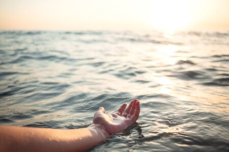 Woman hands in water inviting you over sunset golden rays. Summer vacation and travel conceptの写真素材