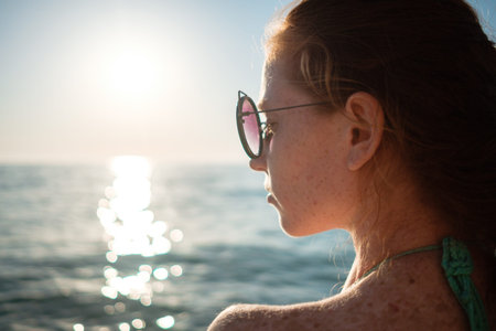 Ginger girl with freckles in a bikini looks at a beautiful sunset over the sea. Idea and concept of...