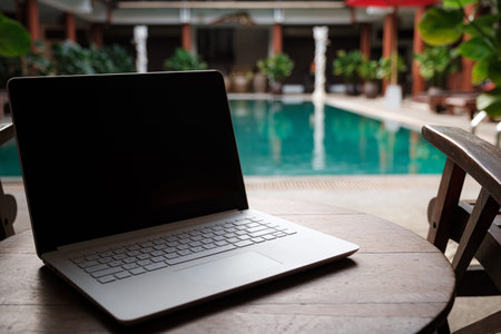 A white laptop on wooden table swiming pool background. A start of new day. Freelance business...
