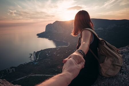 Girl standing on the mountain top over blue sea view. Follow me - POV. Couple enjoying a hike in nature. The concept of the journey to the meeting of new discoveries