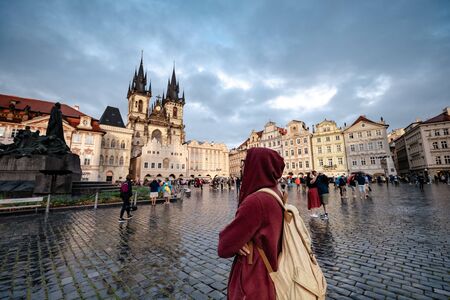 A man with a backpack and a red hoodie looks in surprise at the central square of the city of Prague. The idea and concept of discoveries and travelの写真素材
