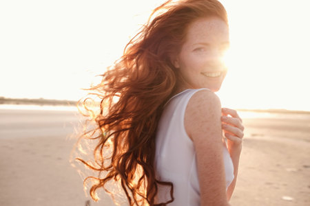 Beautiful young lady with long healthy red hair and cute white dress walking near lake. Hot summer evening. Sunset. Lifestyle concept.の写真素材