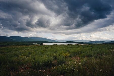 A lake in the valley among the mountains before it rains. Beautiful sunset light. Mountain valley cloudy sky landscape. Green bush.の写真素材