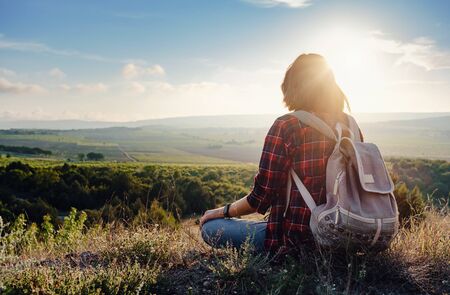 Young hipster girl enjoy sunset on viewpoint. Travel woman with backpack. Enjoying nature sunset. Relaxing in mountains at sunrise. Trekking conceptの写真素材